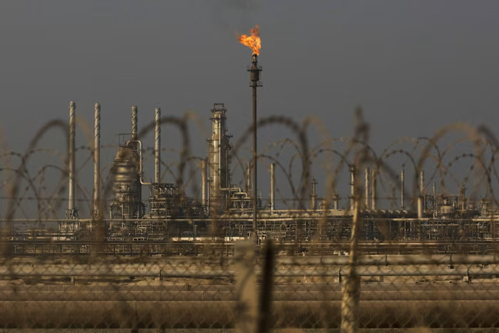 A flame burns atop a tall tower at Saudi Aramco's Ras Tanura oil refinery, seen behind barbed wire fencing.