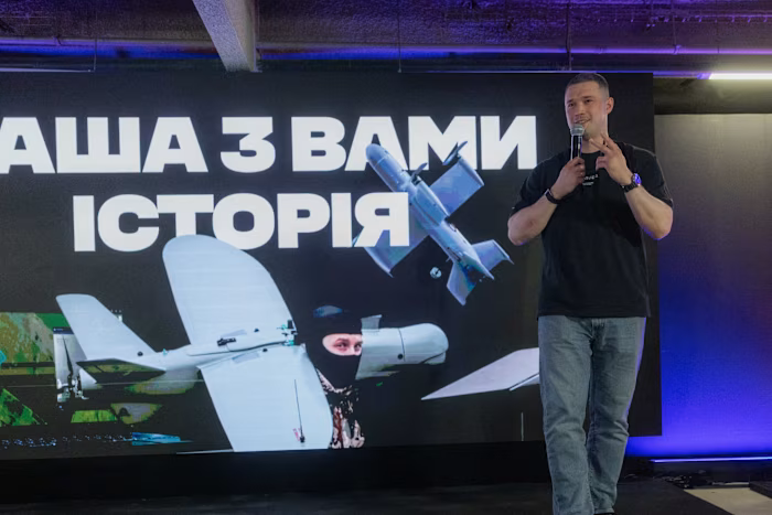 Киев иска от Мъск да одобри използването на дронове със Starlink срещу руски балистични ракетни установки 3 Ukrainian Defence Minister Mykhailo Fedorov stands on stage holding a microphone, speaking in front of a screen displaying drones and Ukrainian text.