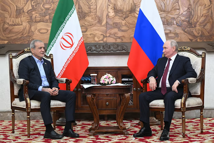 Русия тайно помагала на Иран да разработи свръхзвукови крилати ракети 2 Vladimir Putin and Masoud Pezeshkian sit and talk across a small table, with Russian and Iranian flags behind them.