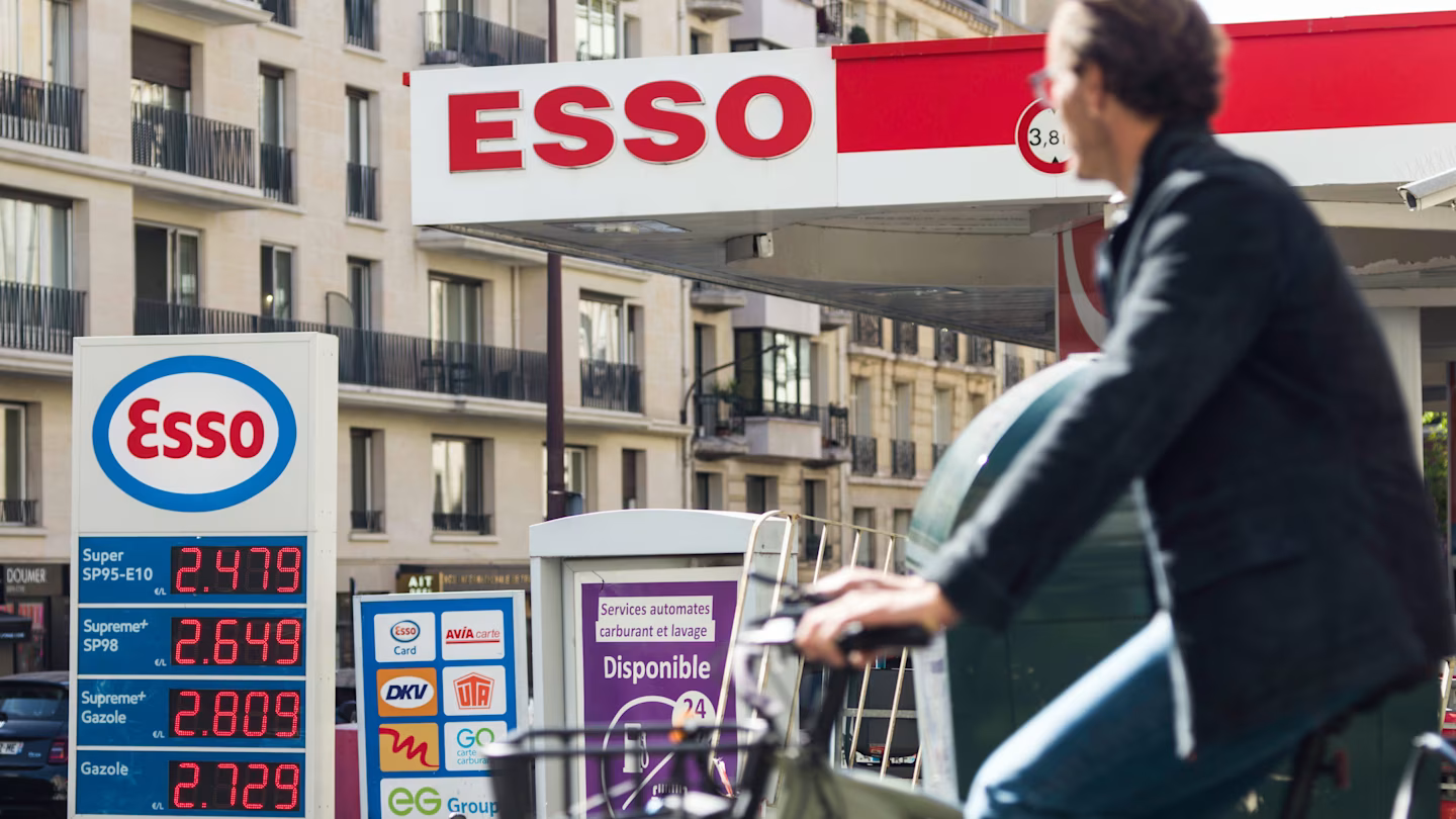 A cyclist passes an Esso petrol station in Paris. Fuel prices are displayed at record highs on the sign.